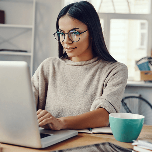 Woman with long, dark hair and glasses working on her laptop at home