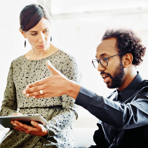 A man and woman looking at a mobile device and having a discussion at work