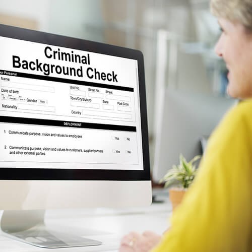 A woman looking at a computer monitor that shows a criminal background check.