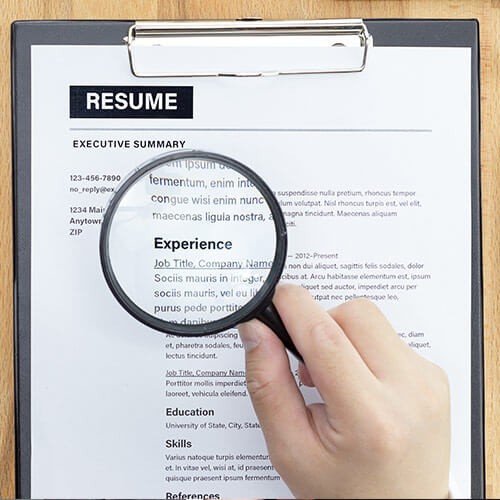 A person holding a magnifying glass over a resume showing job experience.