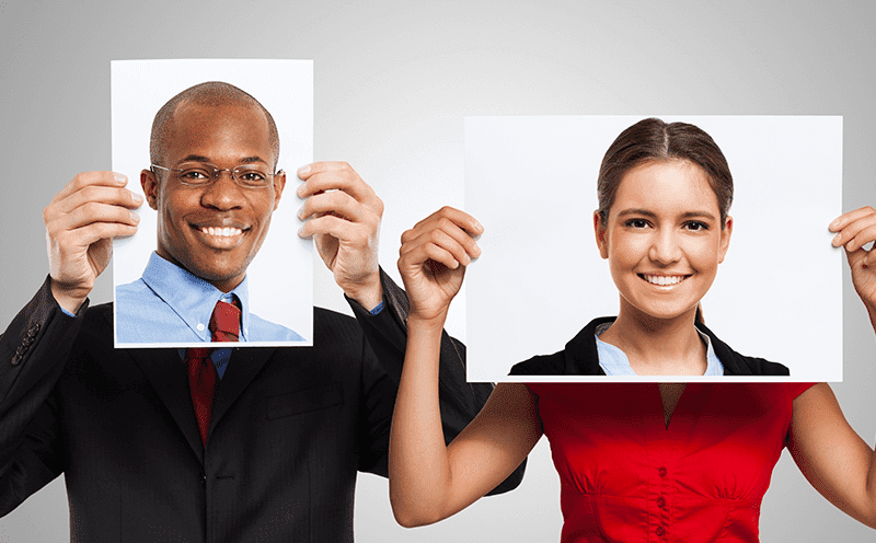 A man and a woman holding photos of different faces in front of their heads