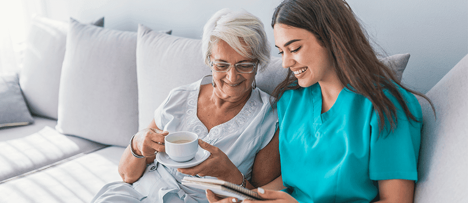 An elderly woman and her caregiver sitting on a couch together